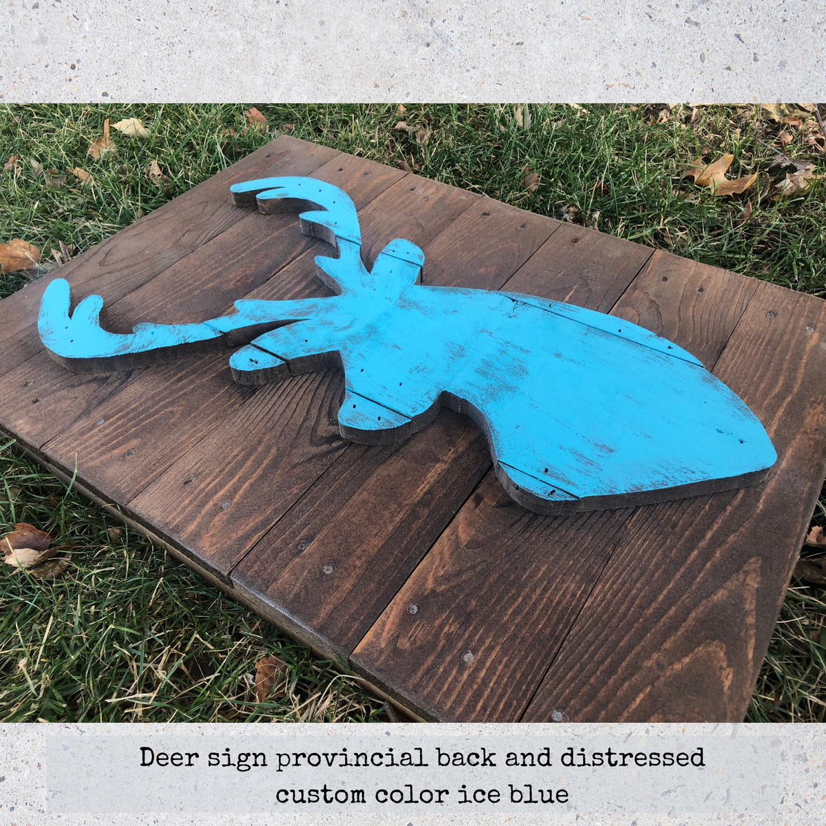 A wooden deer sign with a distressed blue color, placed on a wooden surface.
