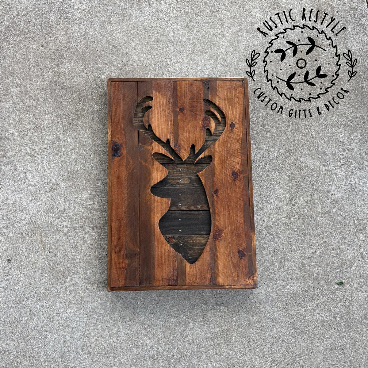 a wooden board with a carved deer head design on it, placed on a concrete surface.