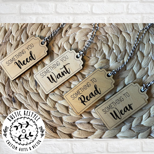 4 Christmas gift tags laying on a woven placemat. First tag says Something you Need. Second tag says Something you Want. Third tag says Something you Read and the last tag says something you Wear. Each tag has a black and white bakers twine string.