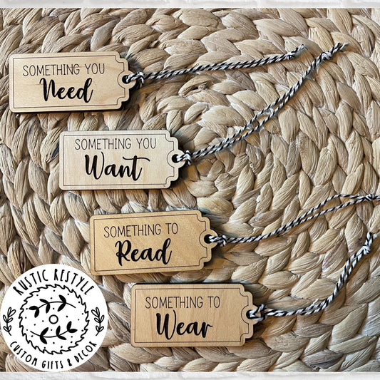 4 Christmas gift tags laying on a woven placemat. First tag says Something you Need. Second tag says Something you Want. Third tag says Something you Read and the last tag says something you Wear. Each tag has a black and white bakers twine string.