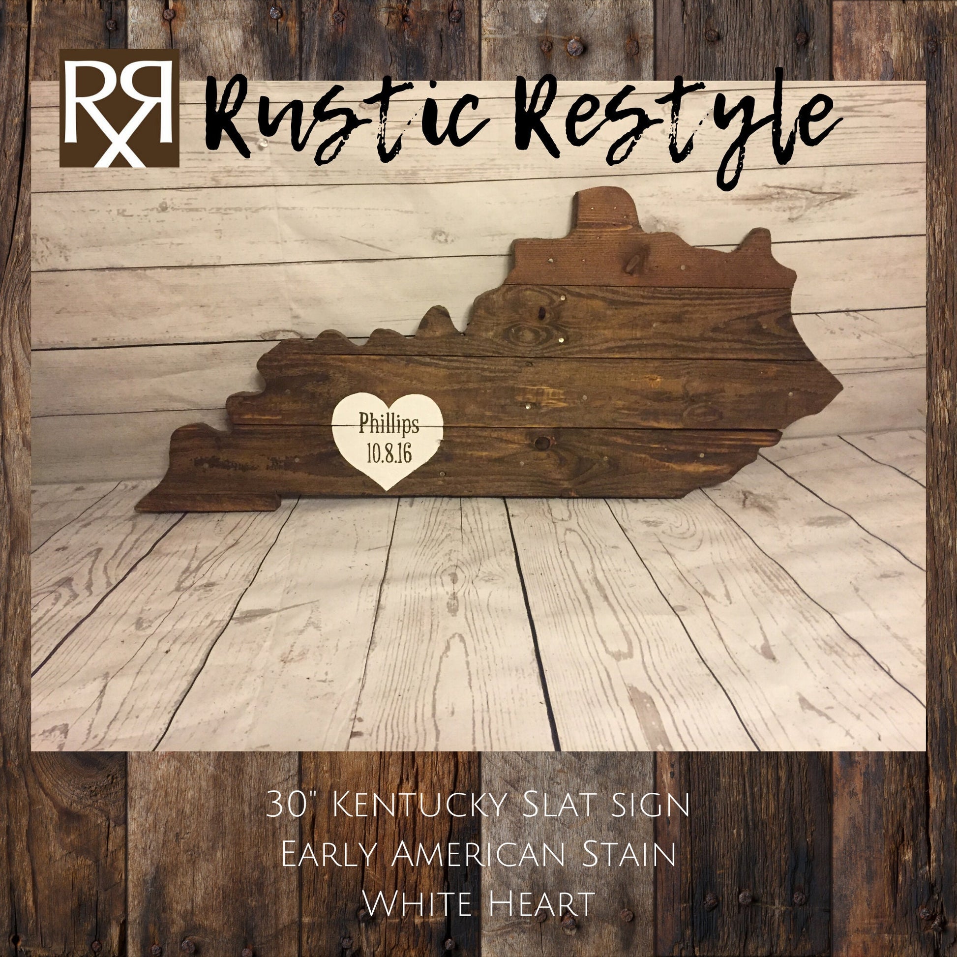 Kentucky-shaped wood sign leaning up against a faux white wood wall. Horizontal wood slats with nail holes showing. A White heart is painted near the lower left with the name Phillips and date painted on it.