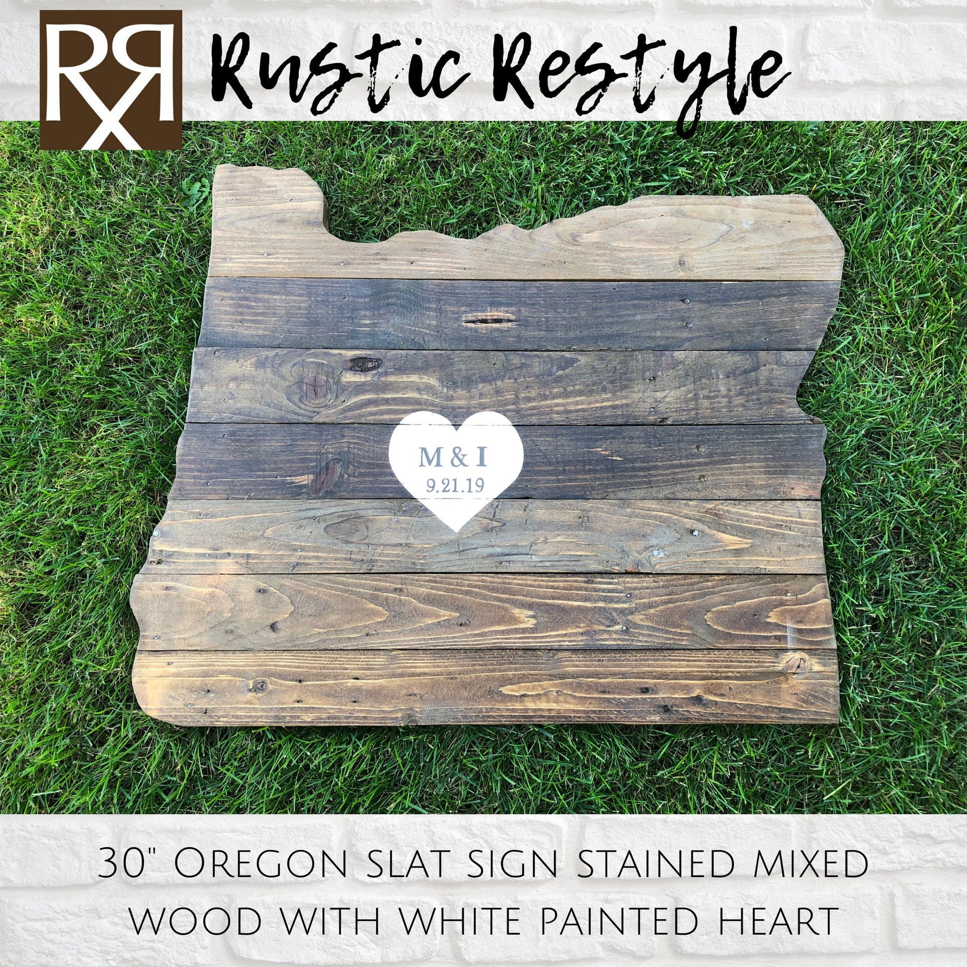 wood sign shaped like Oregon, old dark worn boards with nails laying in the green grass with a  White heart painted in the center with personalization M&L