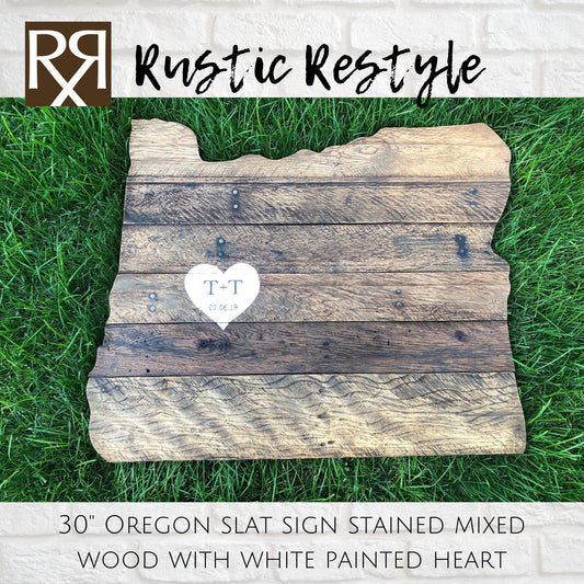 wood sign shaped like Oregon, old dark worn boards with nails laying in the green grass with a  White heart painted in the center with personalization t + t