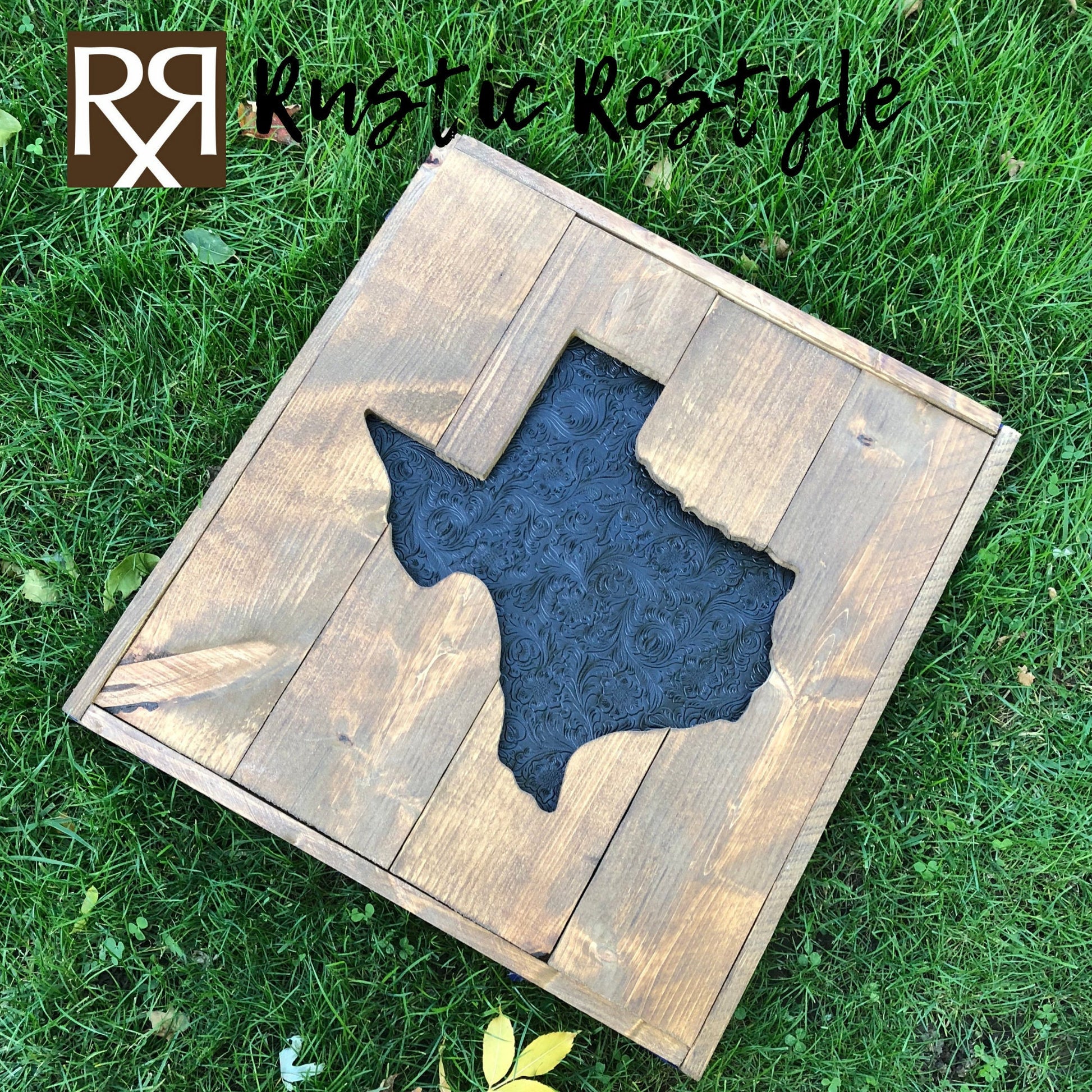Large square wood sign with a texas shape cut out of the middle laying flat in the grass at an angle. The center Texas is recessed in and covered in faux black tooled leather.