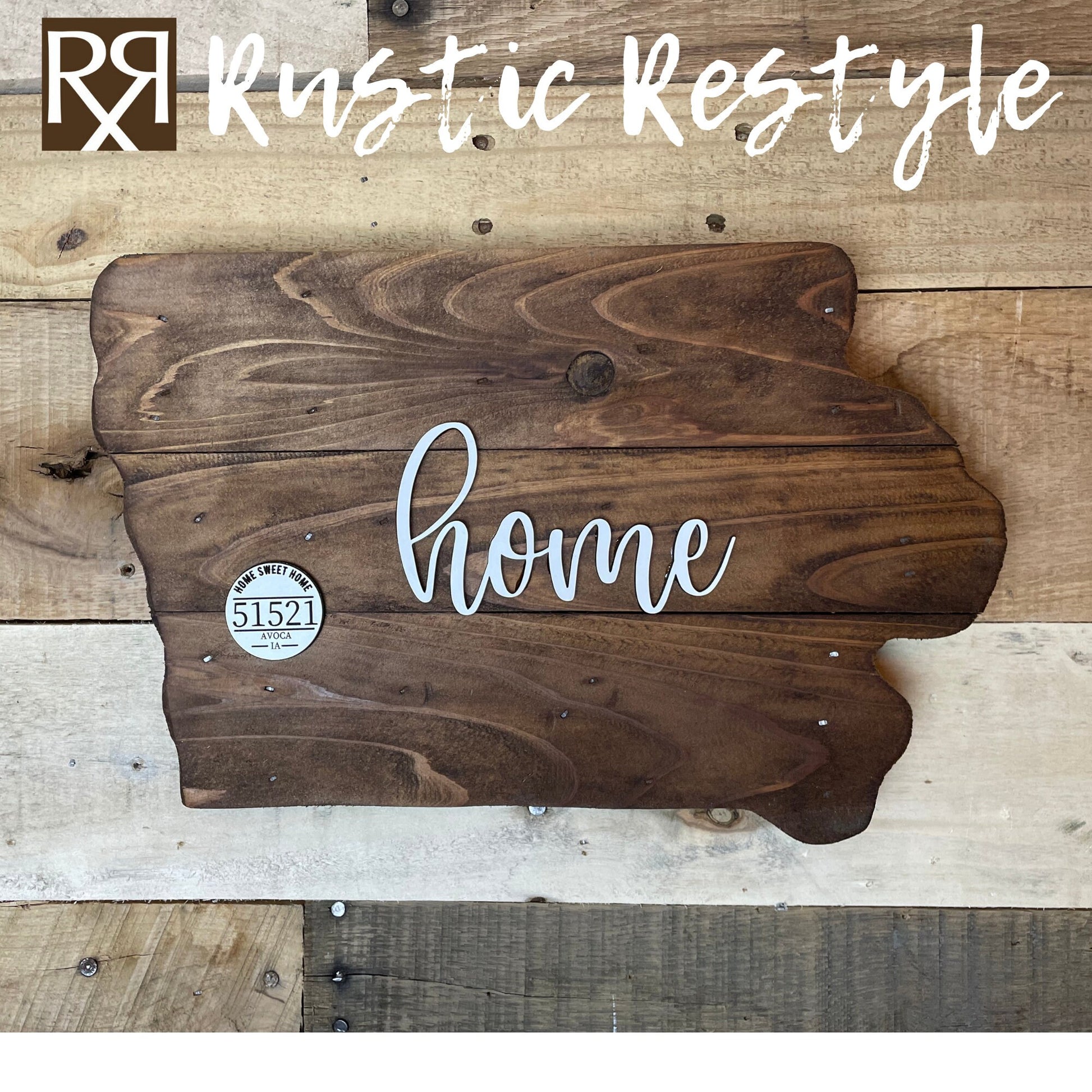 Wooden Iowa shape sign, top view on a flat table. The word home is across the middle in white. There is a small white wooden disc on the left middle with home sweet home, 51521 zip code and Avoca engraved on it.