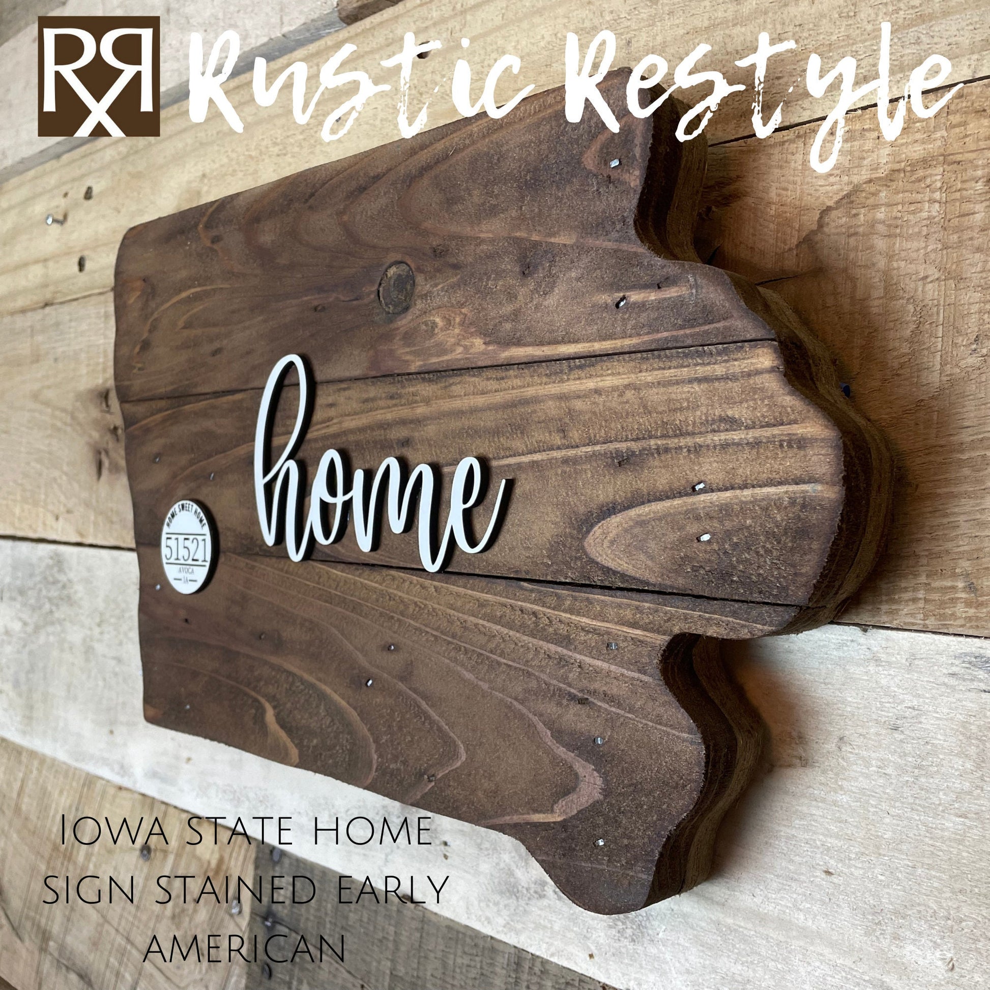 Wooden Iowa shape sign, right side view on a flat table. The word home is across the middle in white. There is a small white wooden disc on the left middle with home sweet home, 51521 zip code and Avoca engraved on it.