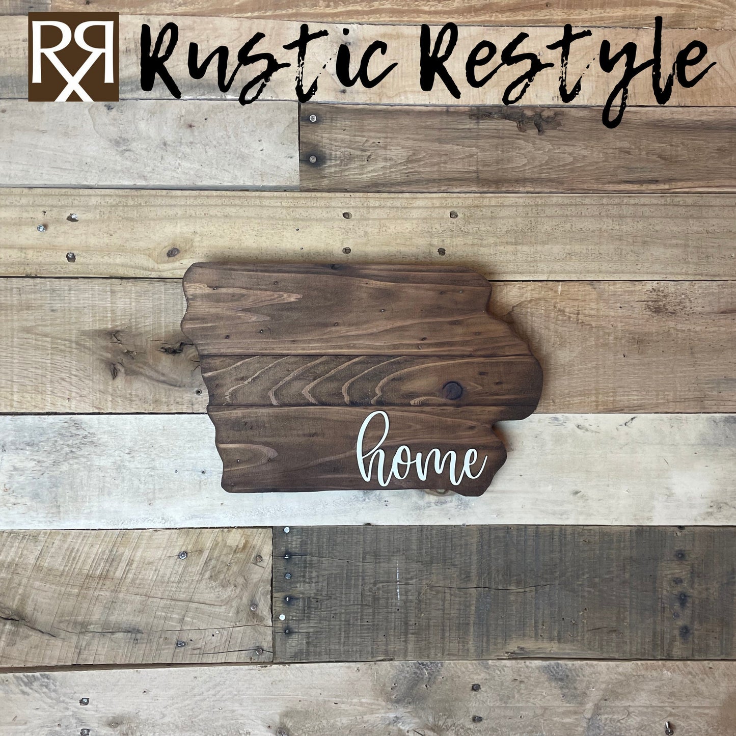 Iowa shaped wood sign with dark planks.
Script font white word "home" in the bottom right corner. The sign is hanging on a wood pallet plank wall.