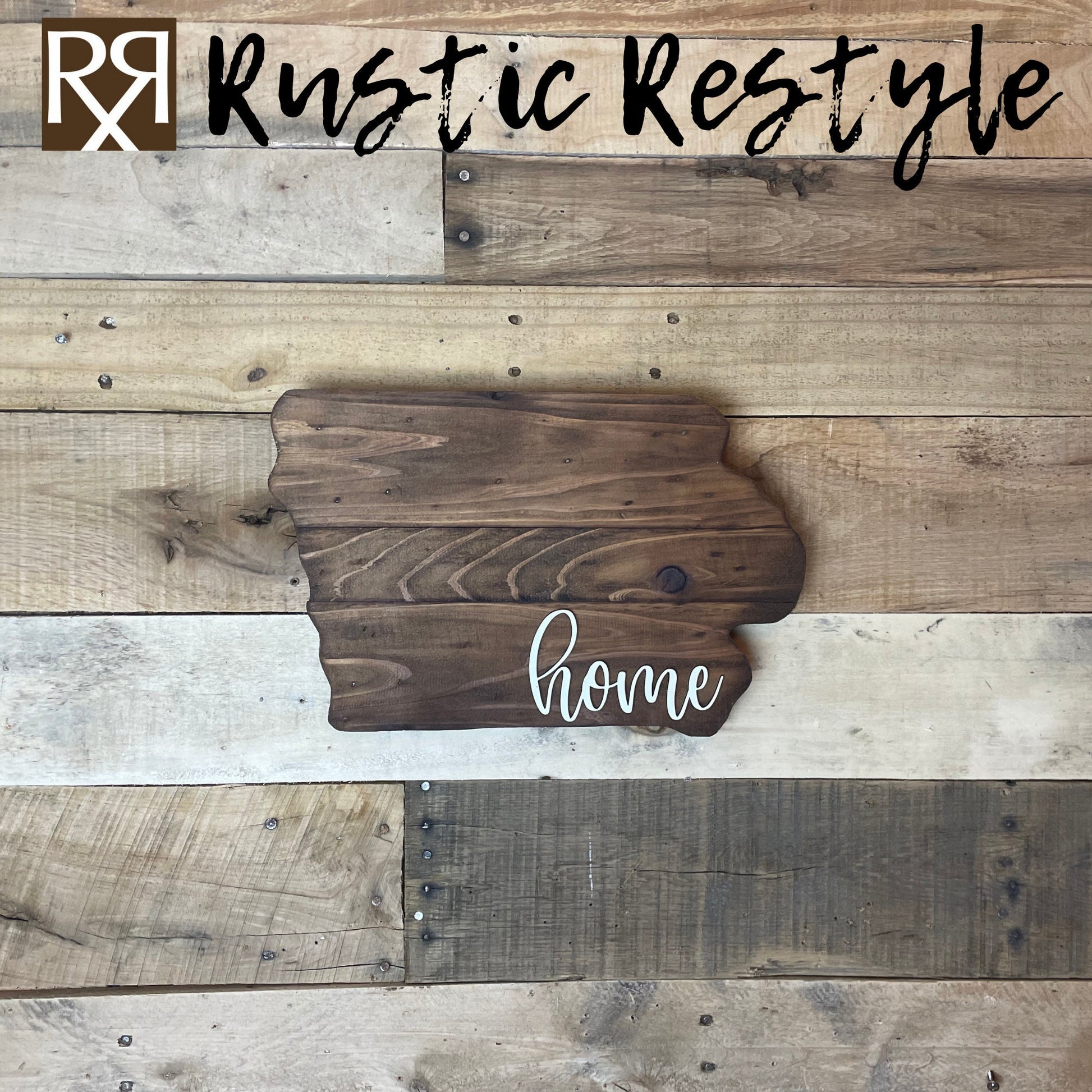 Iowa shaped wood sign with dark planks.
Script font white word "home" in the bottom right corner. The sign is hanging on a wood pallet plank wall.
