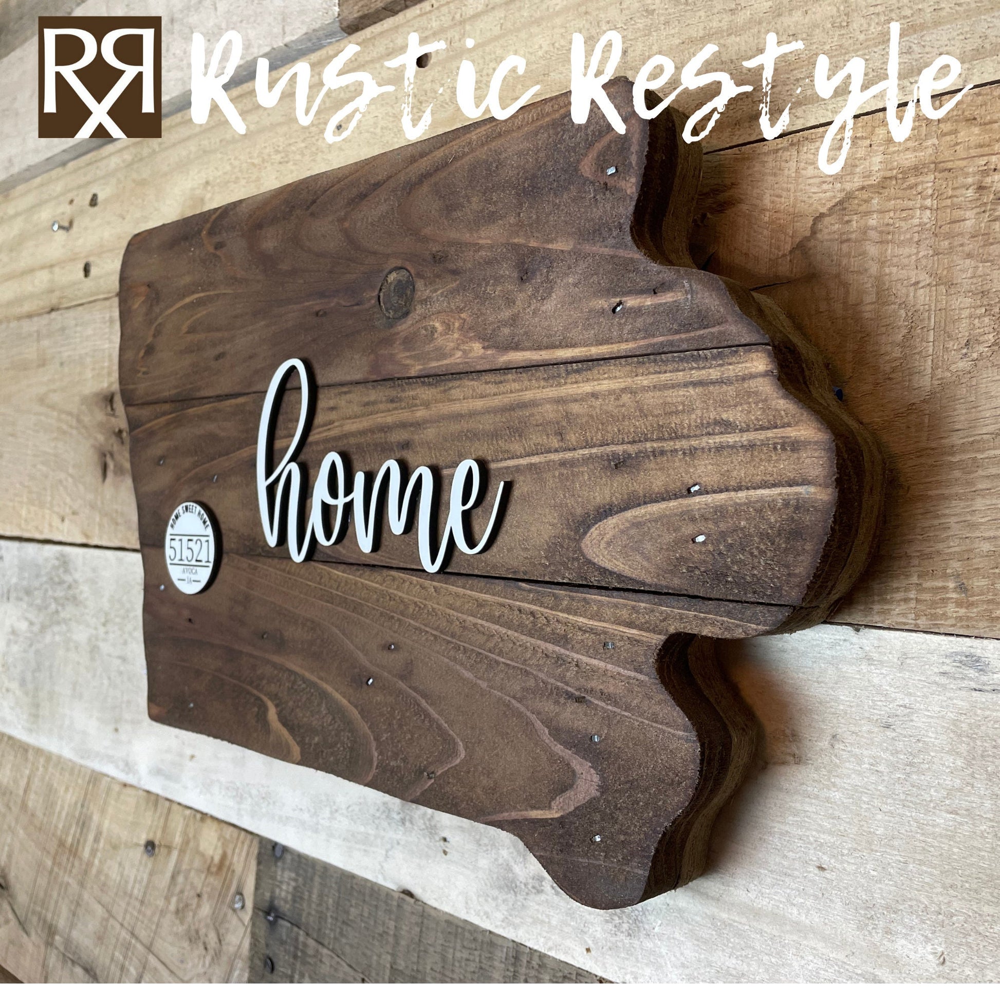 Wooden Iowa shape sign, right side view on a flat table. The word home is across the middle in white. There is a small white wooden disc on the left middle with home sweet home, 51521 zip code and Avoca engraved on it.
