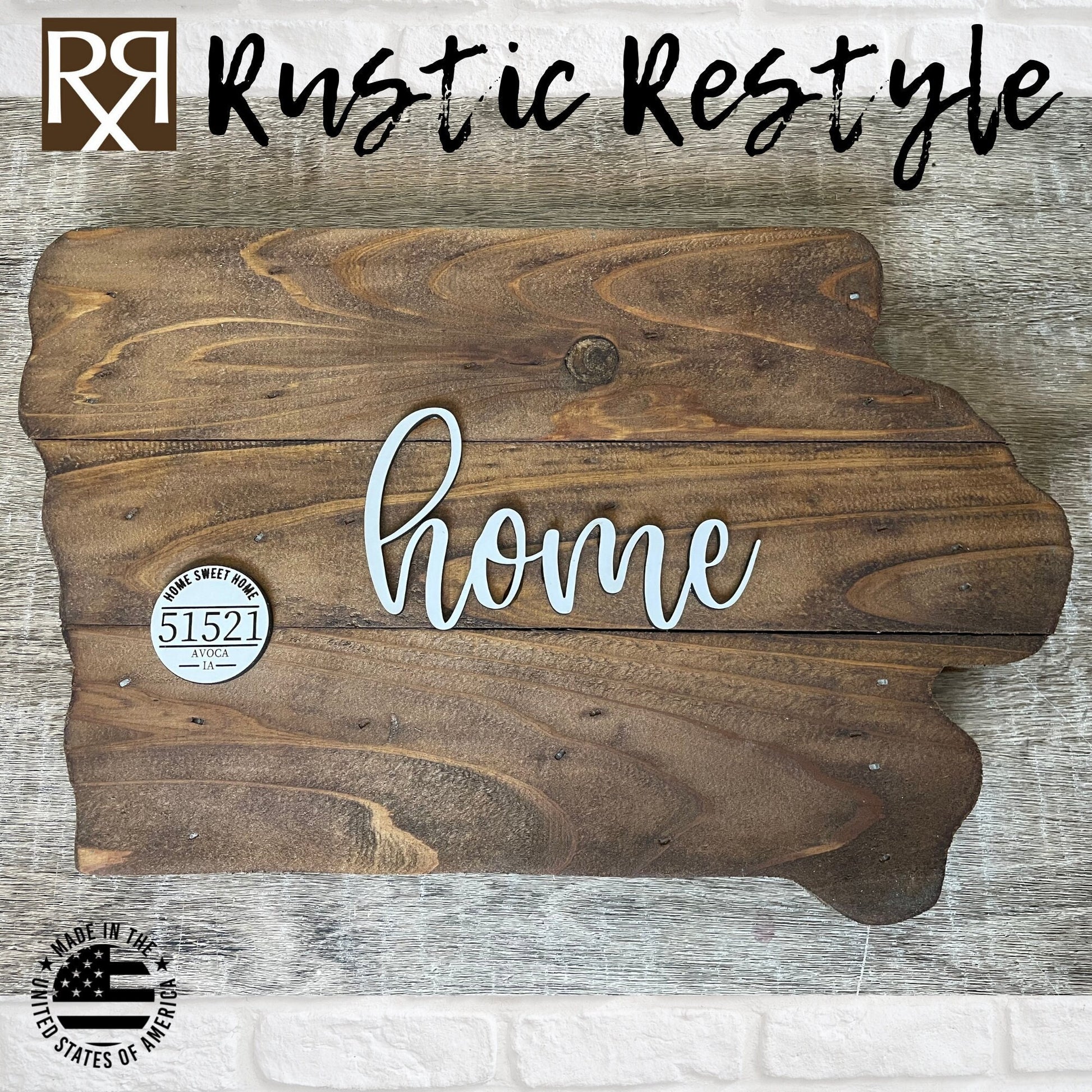 Wooden Iowa shape sign, top view on a flat table. The word home is across the middle in white. There is a small white wooden disc on the left middle with home sweet home, 51521 zip code and Avoca engraved on it.