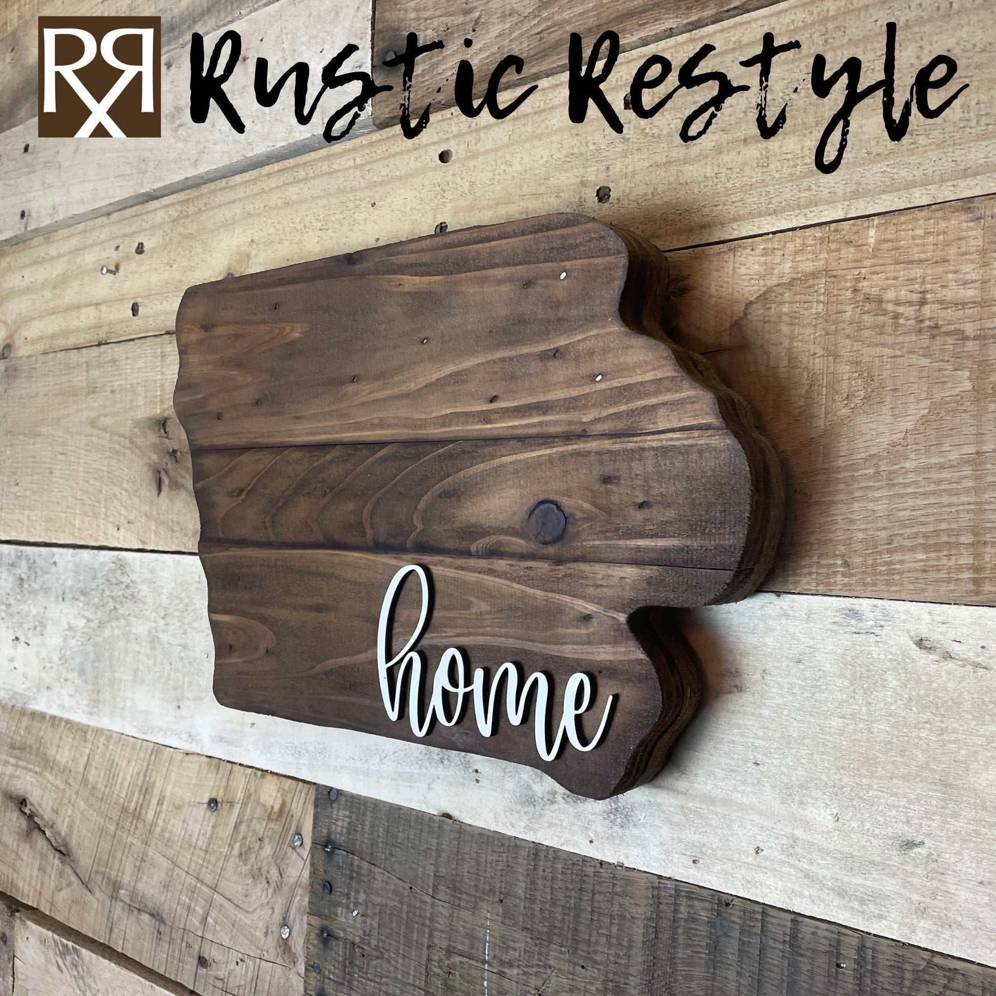 A side angle view of iowa shaped wood sign with dark planks.
Script font white word "home" in the bottom right corner. The sign is hanging on a wood pallet plank wall.