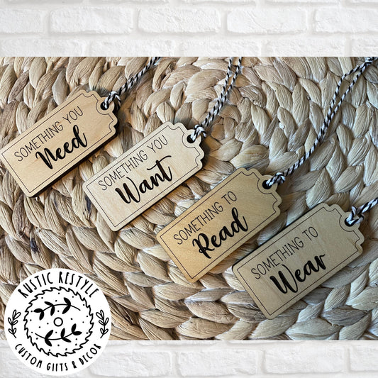 4 Christmas gift tags laying on a woven placemat. First tag says Something you Need. Second tag says Something you Want. Third tag says Something you Read and the last tag says something you Wear. Each tag has a black and white bakers twine string.