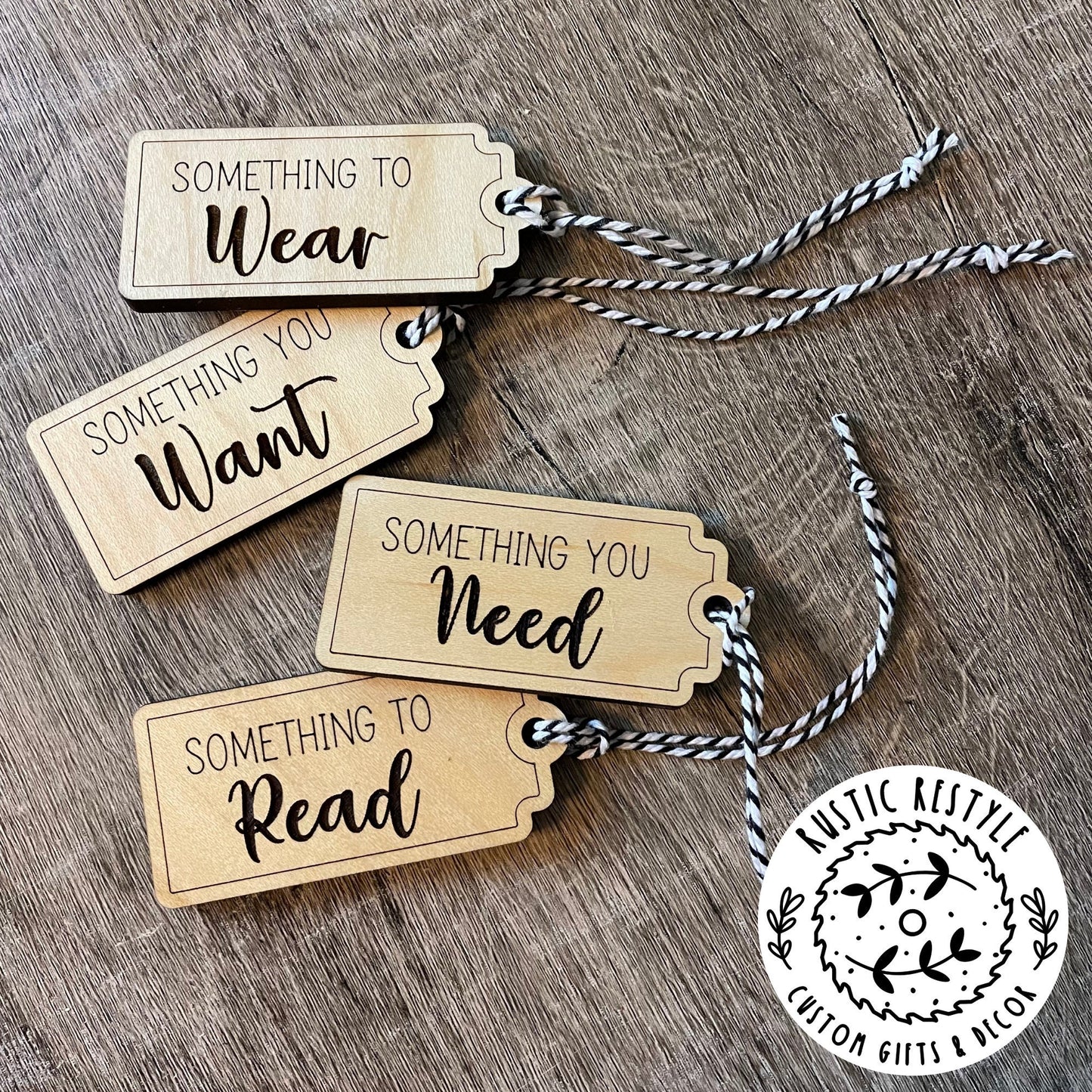 4 Christmas gift tags laying on a wooden table. First tag says Something you Need. Second tag says Something you Want. Third tag says Something you Read and the last tag says something you Wear. Each tag has a black and white bakers twine string.
