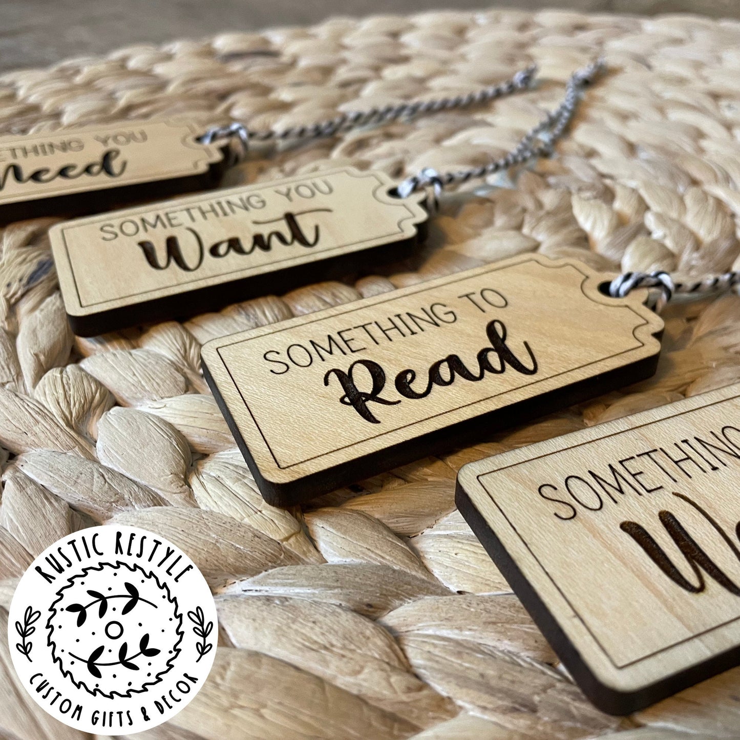 4 Christmas gift tags laying on a woven placemat. First tag says Something you Need. Second tag says Something you Want. Third tag says Something you Read and the last tag says something you Wear. Each tag has a black and white bakers twine string.