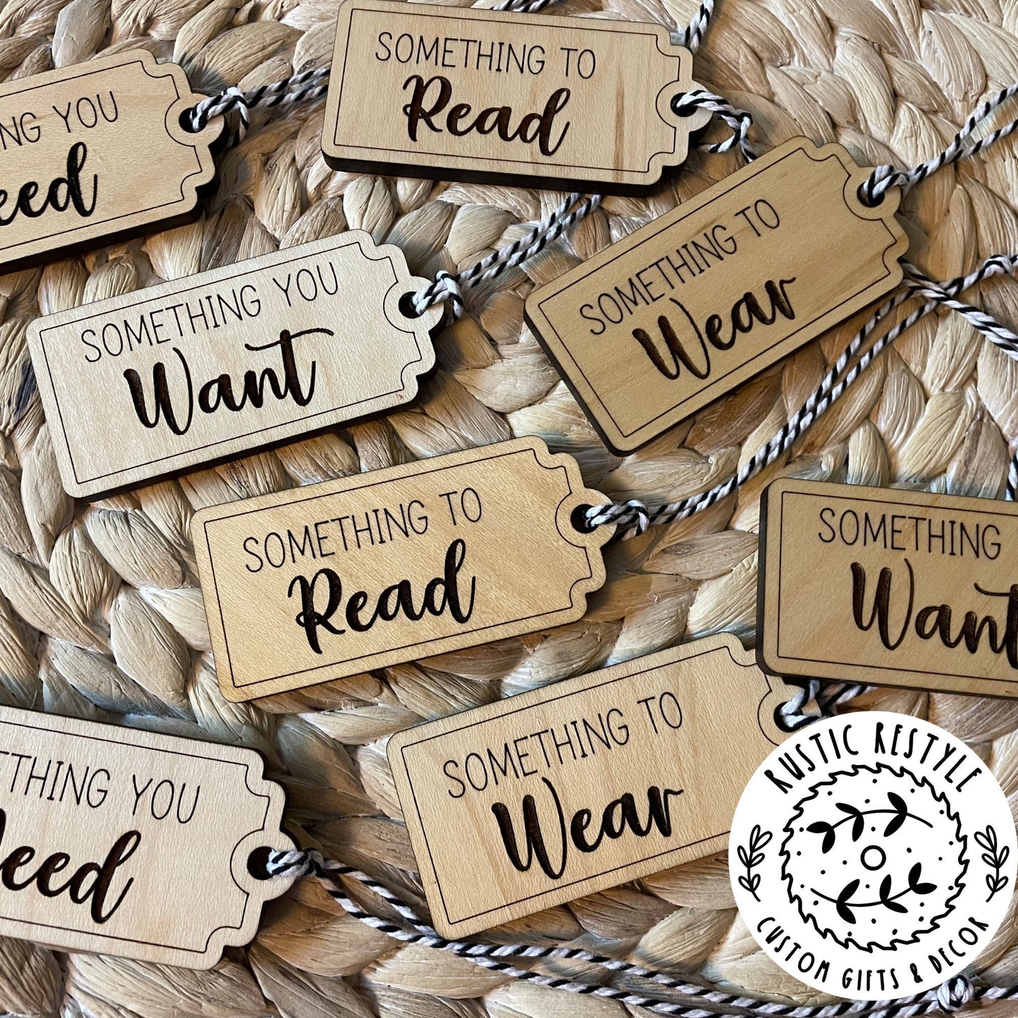 A pile of Christmas gift tags laying on a woven placemat. A mix of 4 sayings, Something to : Want, Wear, Read, and Need. Each tag has a black and white bakers twine string.