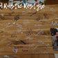 Graduation Guestbook, Large wood rectangle board laying flat on a table. The board has a senior photo in the lower right corner with the name Adryan above it.The board is covered in black and white signatures.