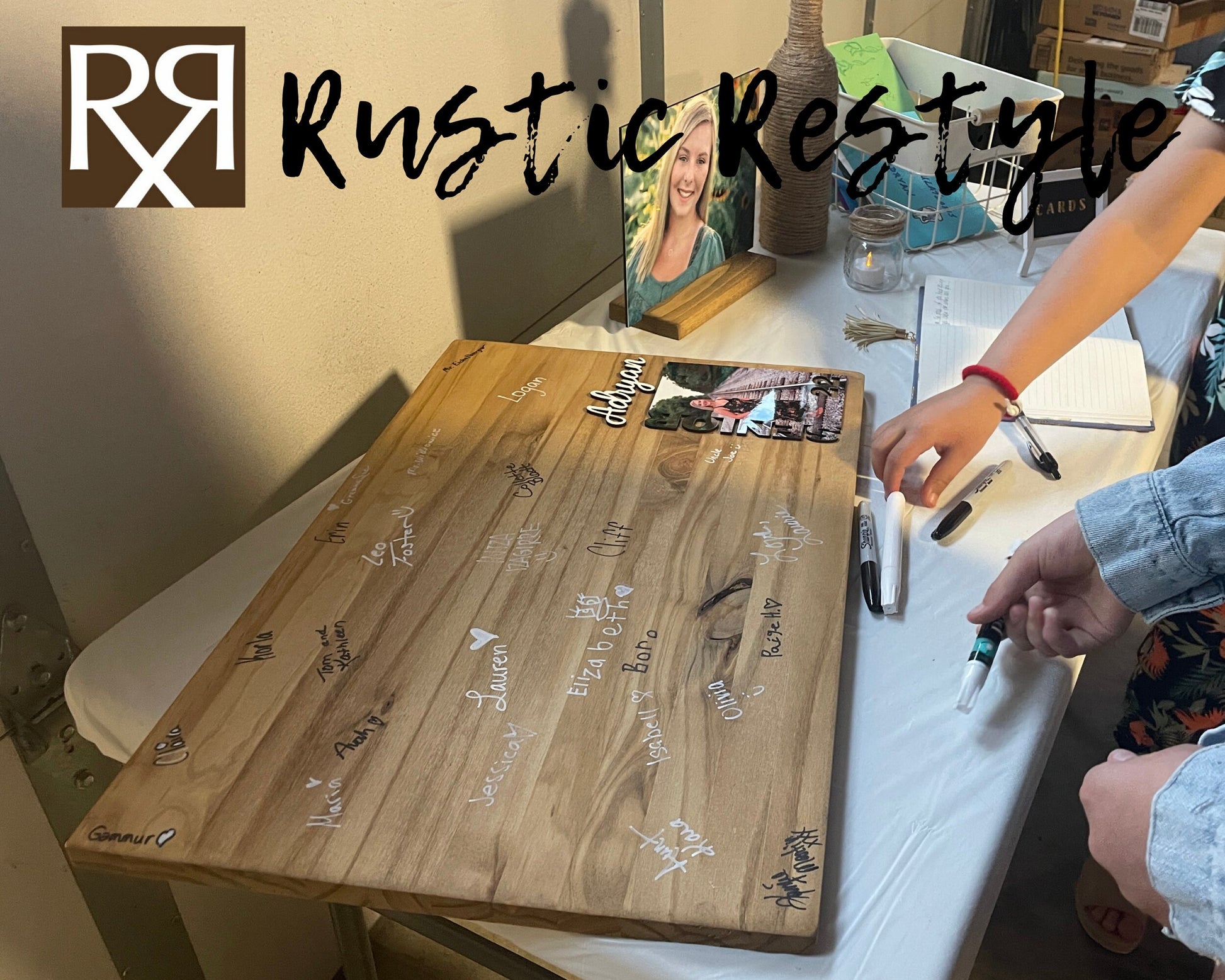 Graduation Guestbook, Side view of Large wood rectangle board laying flat on a table. The board has a senior photo in the lower right corner with the name Adryan above it. The board is covered in black and white signatures.