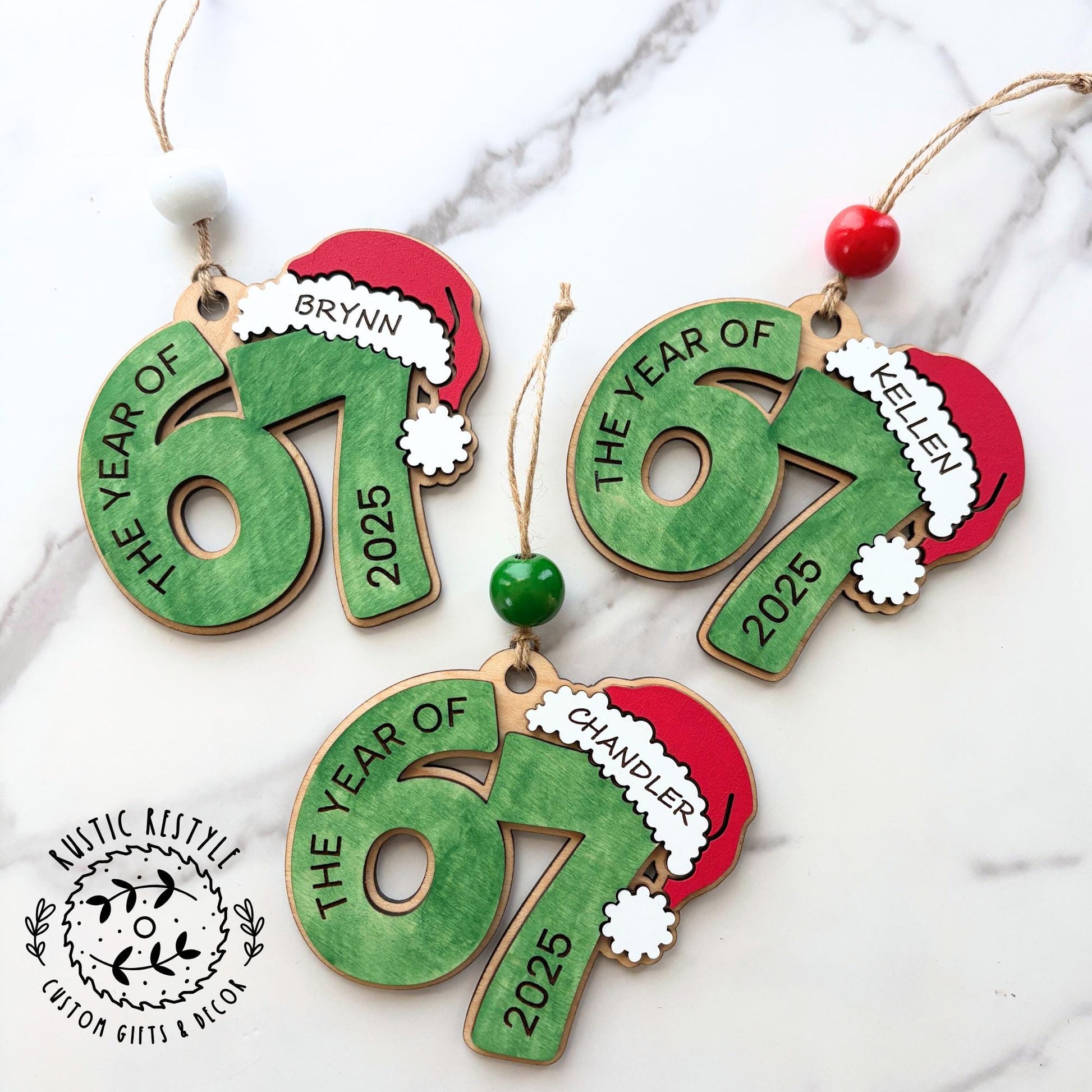 Personalized wooden “67” Christmas ornament with Santa hat, custom name engraving, painted red, green, and white, with beads and hanging string.