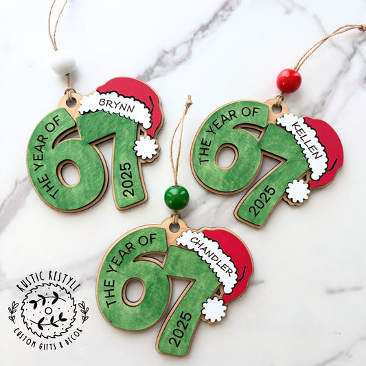 Personalized wooden “67” Christmas ornament with Santa hat, custom name engraving, painted red, green, and white, with beads and hanging string.