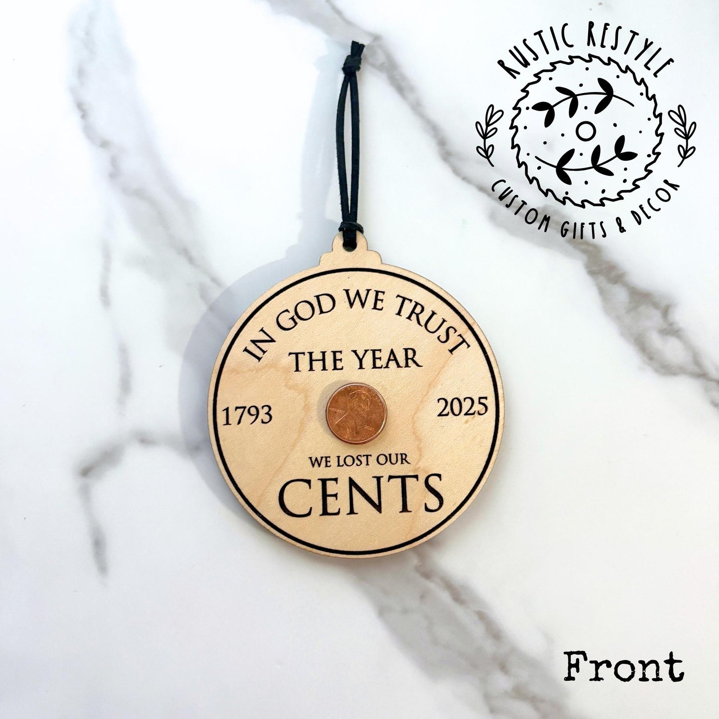 Wooden circular ornament with an embedded penny and engraved text referencing the final penny minted in 2025, hanging on a black cord.