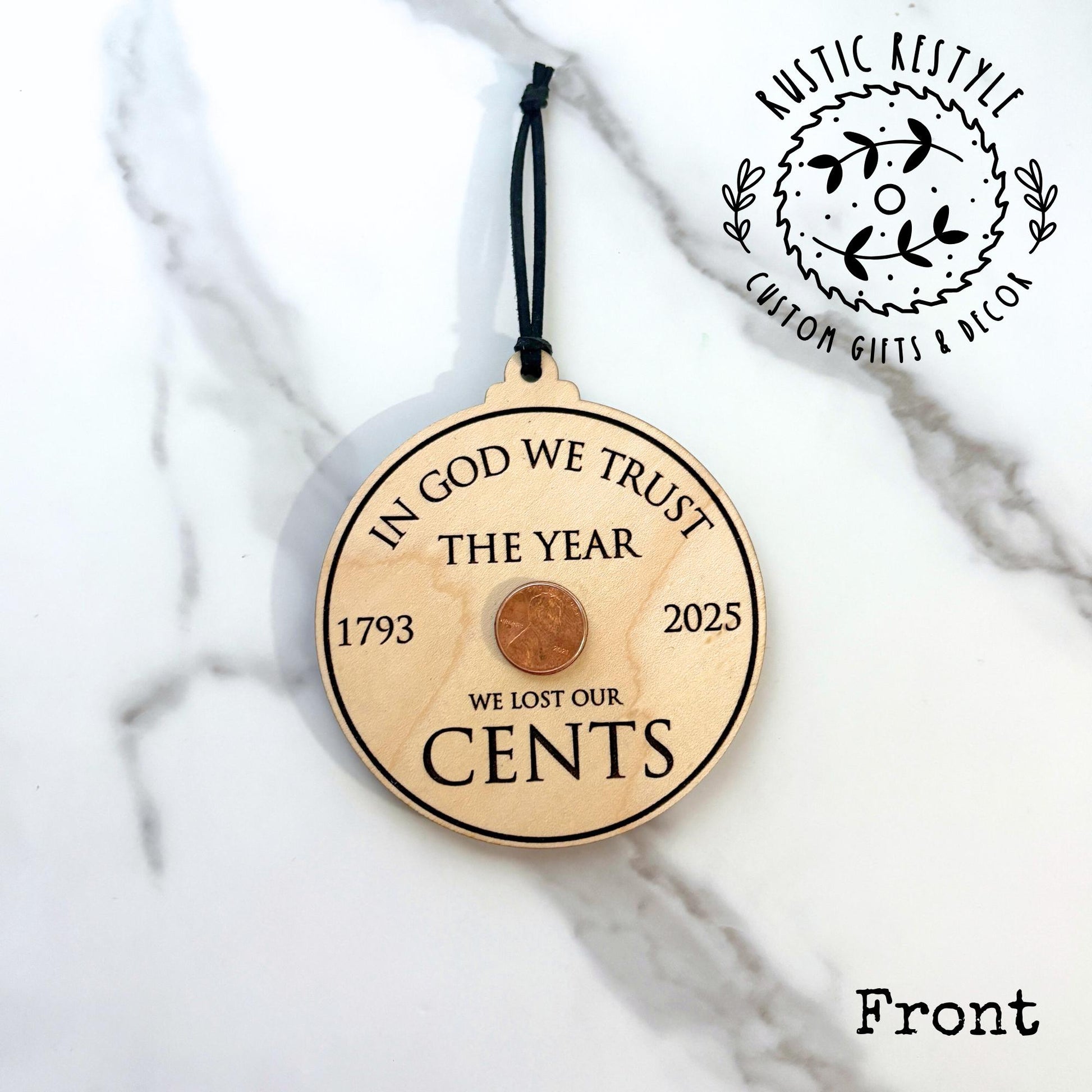 Wooden circular ornament with an embedded penny and engraved text referencing the final penny minted in 2025, hanging on a black cord.
