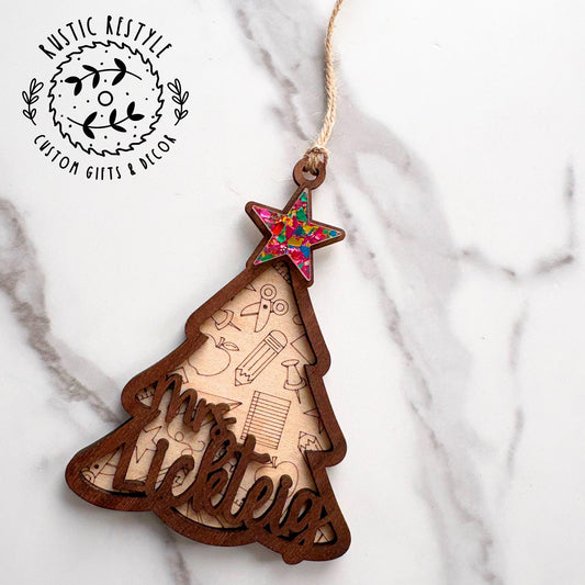Wooden Christmas tree ornament with engraved school icons and a personalized teacher name, topped with a colorful star and twine hanger.
