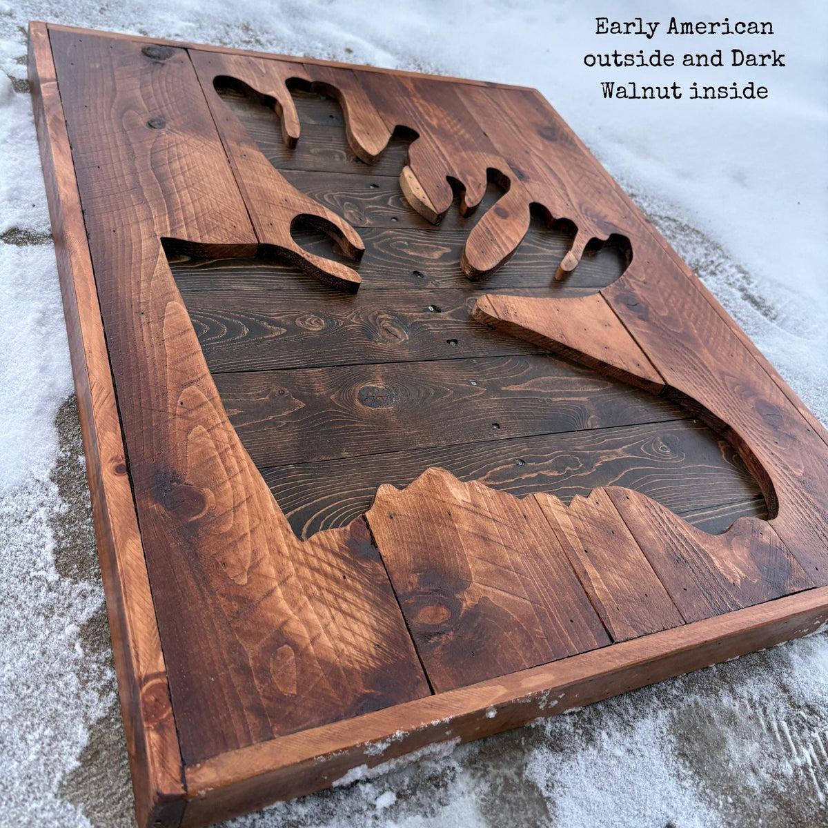 a wooden sign with a carved design, likely depicting a moose, set against a snowy background.