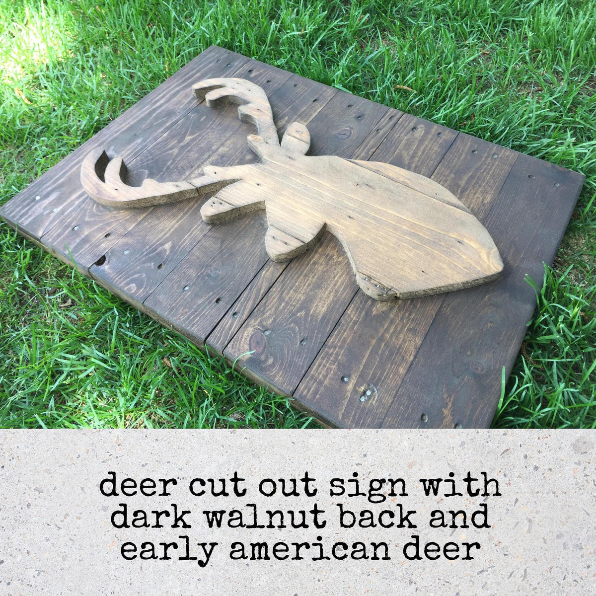 A wooden deer cut out sign with a dark walnut back and early american deer design, placed on a wooden board on a grassy area.