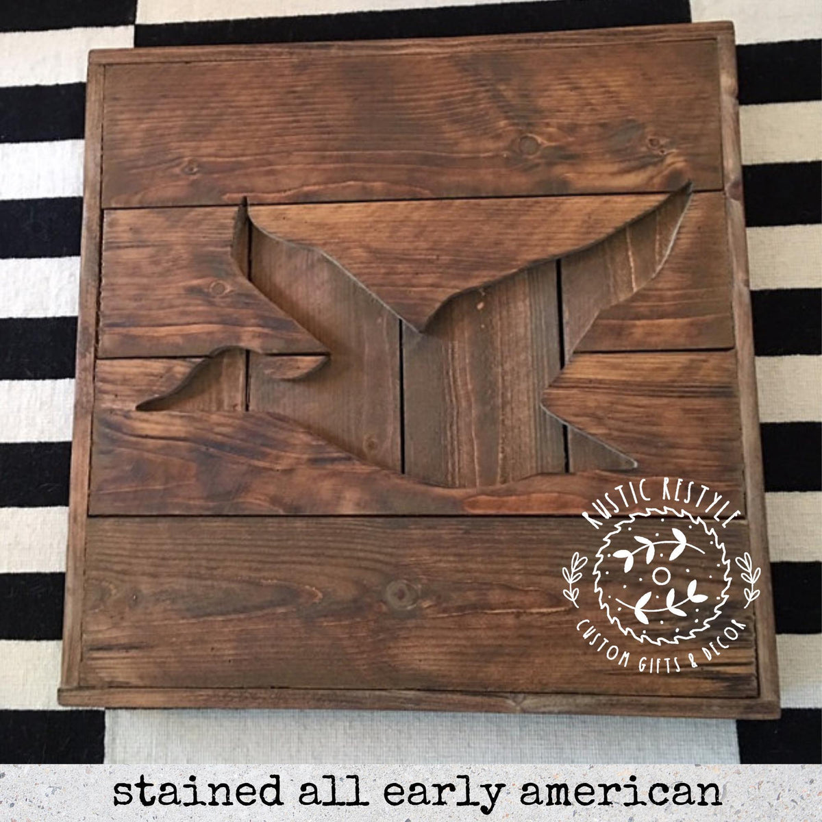 A wooden sign with a bird silhouette cut out of the wood, sitting on a black and white striped surface.