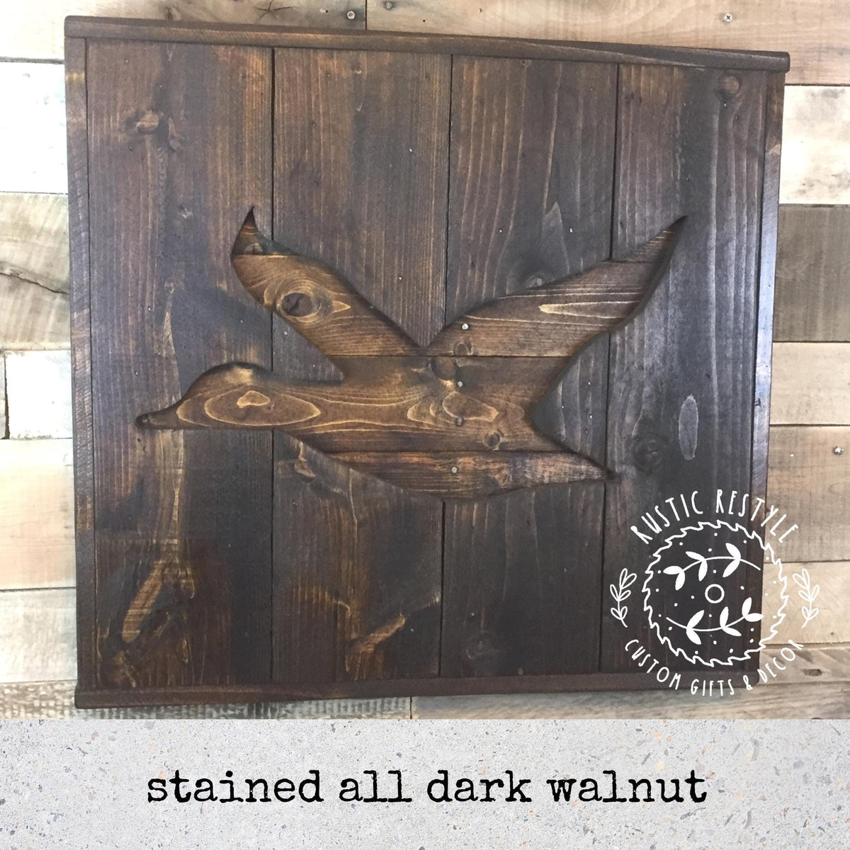 A wooden sign with a carved bird design, likely a duck, in a dark wood color. The sign appears to be stained and has a rustic style.
