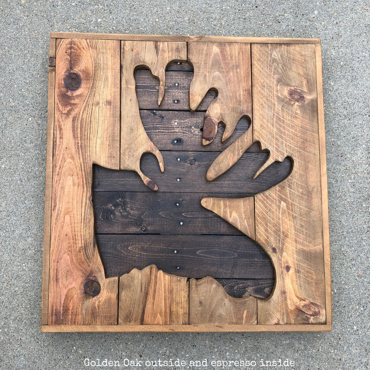 A wooden sign with a moose head cut out from the wood, sitting on a concrete surface.