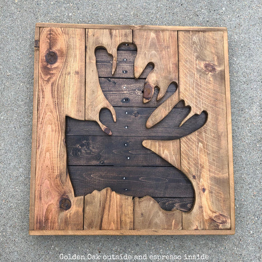 A wooden sign with a moose head cut out from the wood, sitting on a concrete surface.