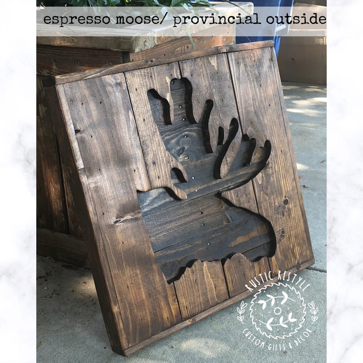 a wooden sign with a moose cutout, sitting on a concrete surface.
