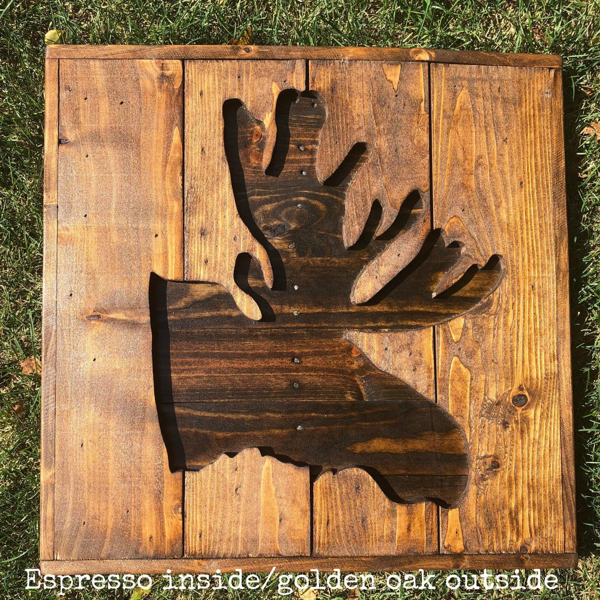 a wooden sign with a moose silhouette cut out, placed on a grassy surface.