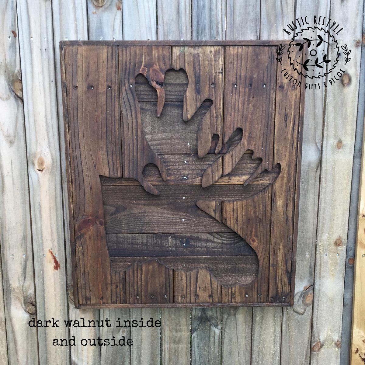 a wooden sign with a carved moose silhouette, mounted on a wooden fence.