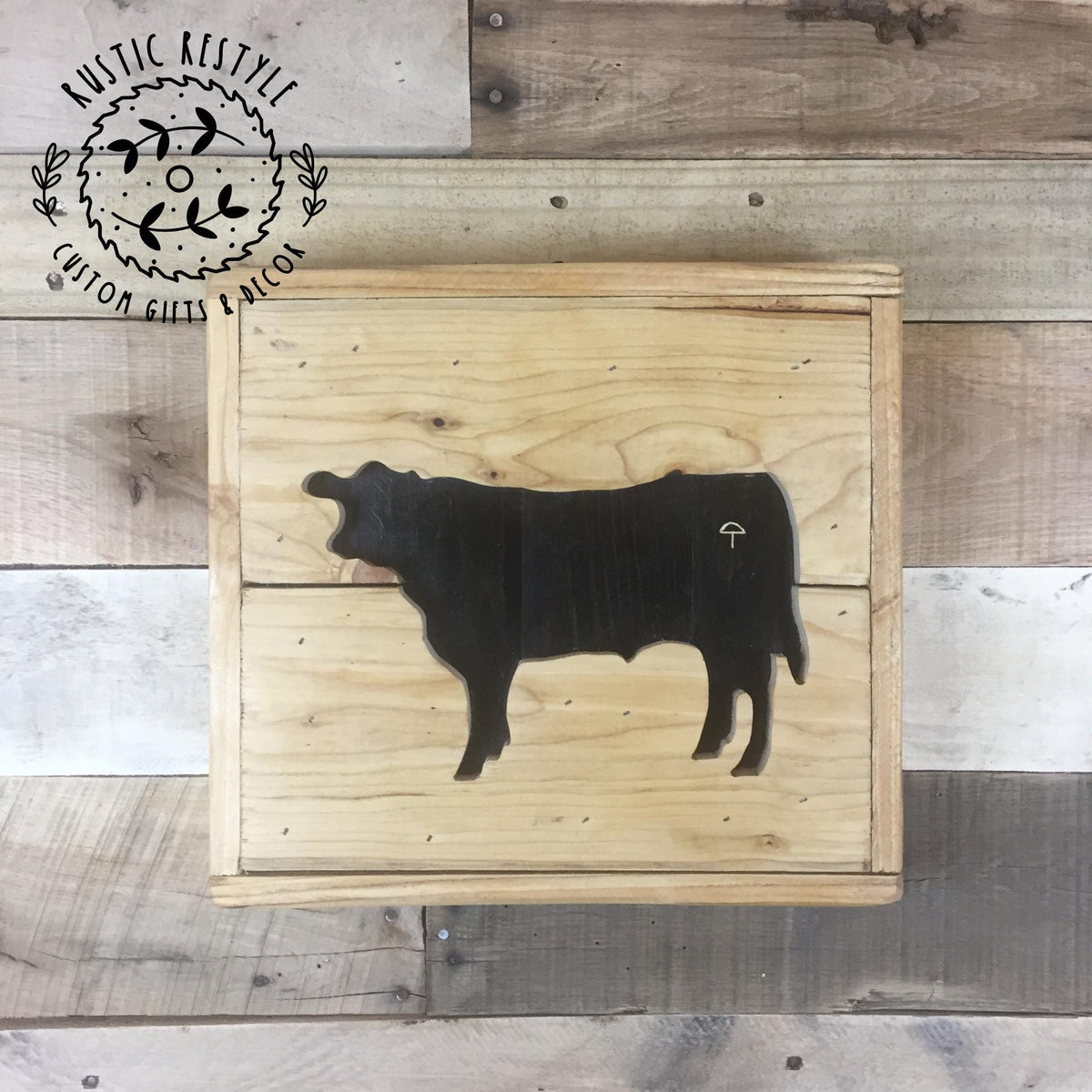 a wooden box with a silhouette of a cow on it, placed on a wooden surface.