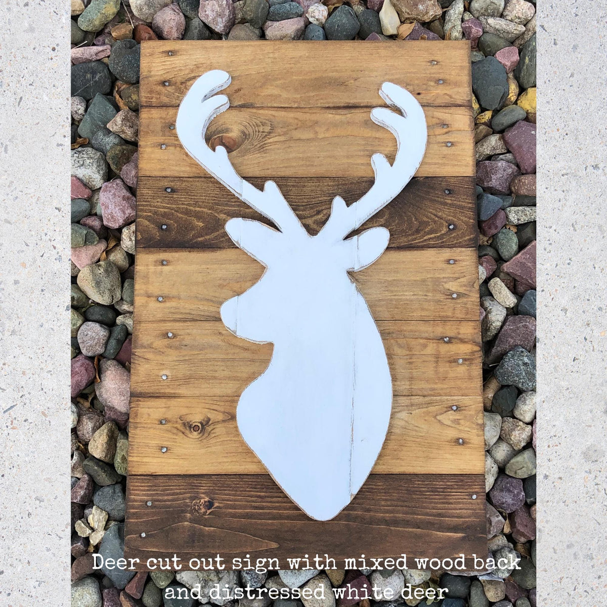 A wooden sign with a white deer head silhouette is displayed on a bed of rocks.
