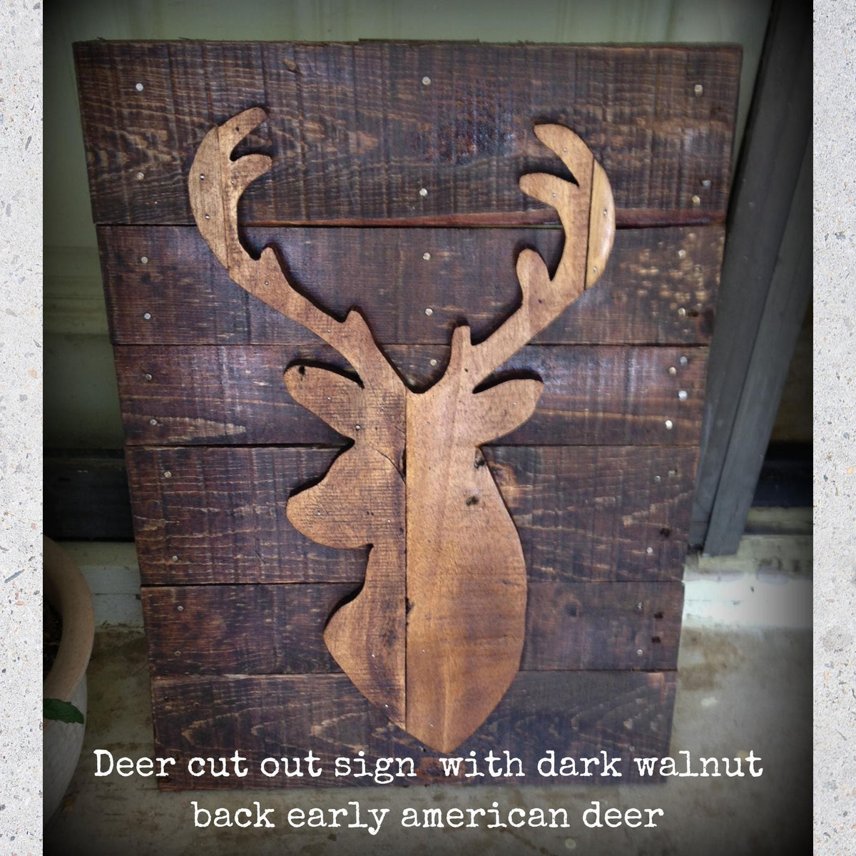 A wooden deer head cut out from a dark walnut, mounted on a wooden board.