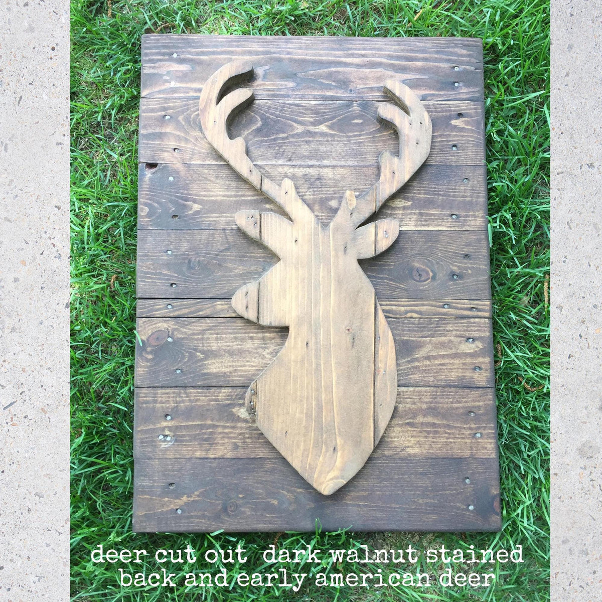 A wooden deer head cut out from a dark-colored wood plank, with the deer's antlers visible, resting on a grassy surface.