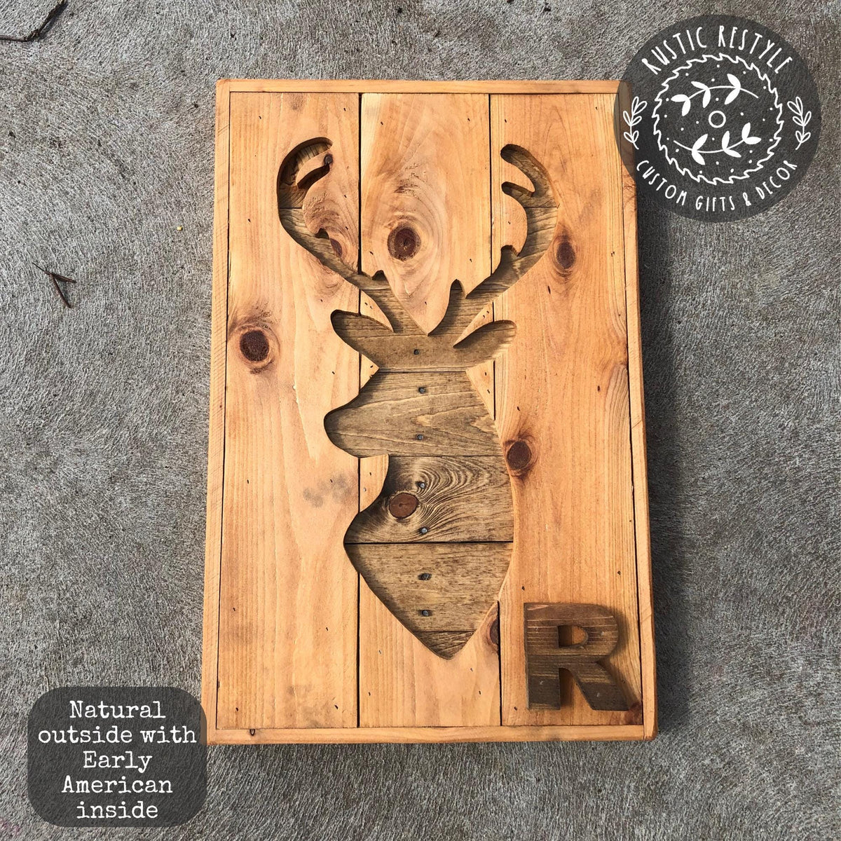 A wooden sign with a carved deer head and the letter "R" on it, placed on a concrete surface.