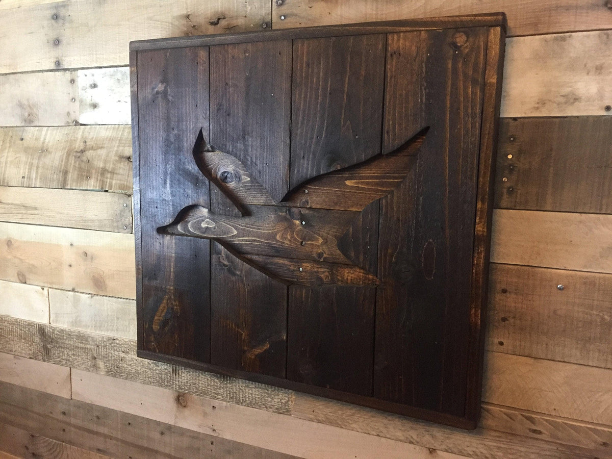 a wooden panel with a carved bird design on it, mounted on a wooden wall.