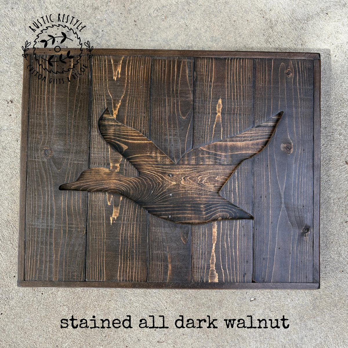 A wooden sign with a bird-like design carved into it, made of dark wood with a stained appearance.