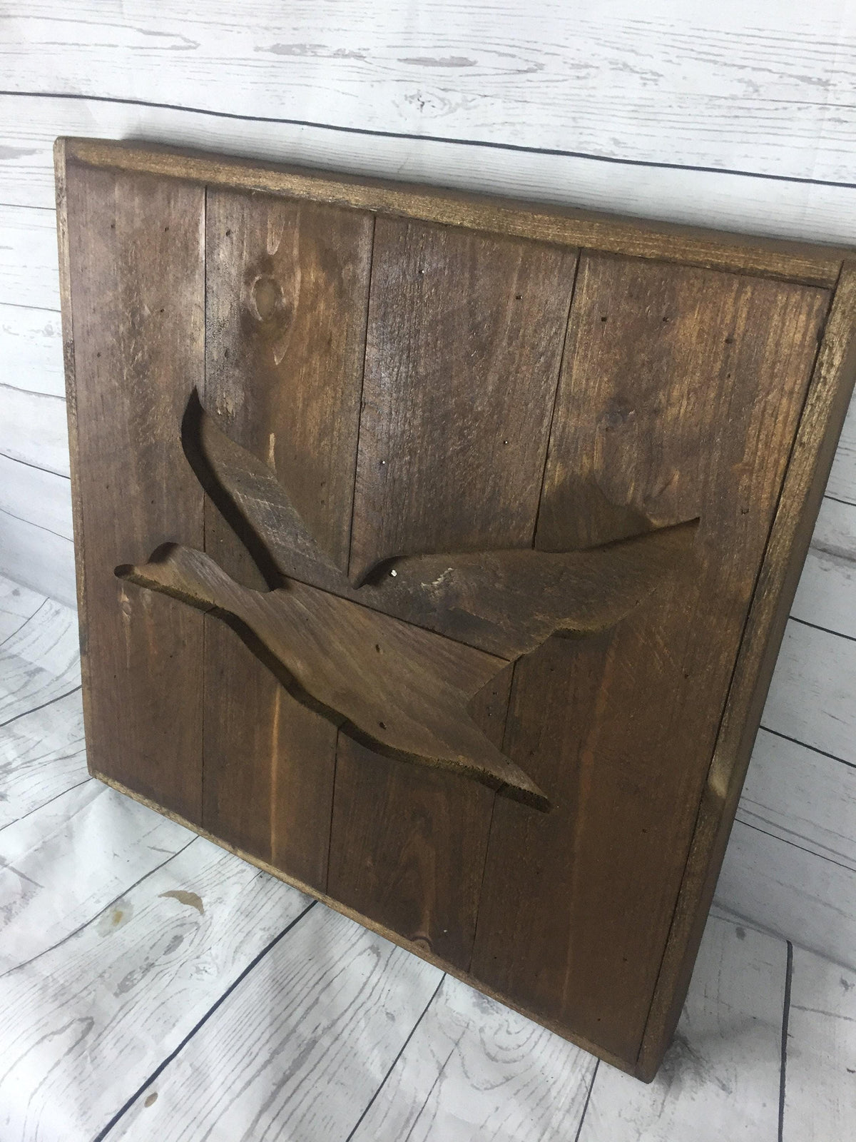 A wooden sign with a carved bird design on it, sitting on a wooden surface.