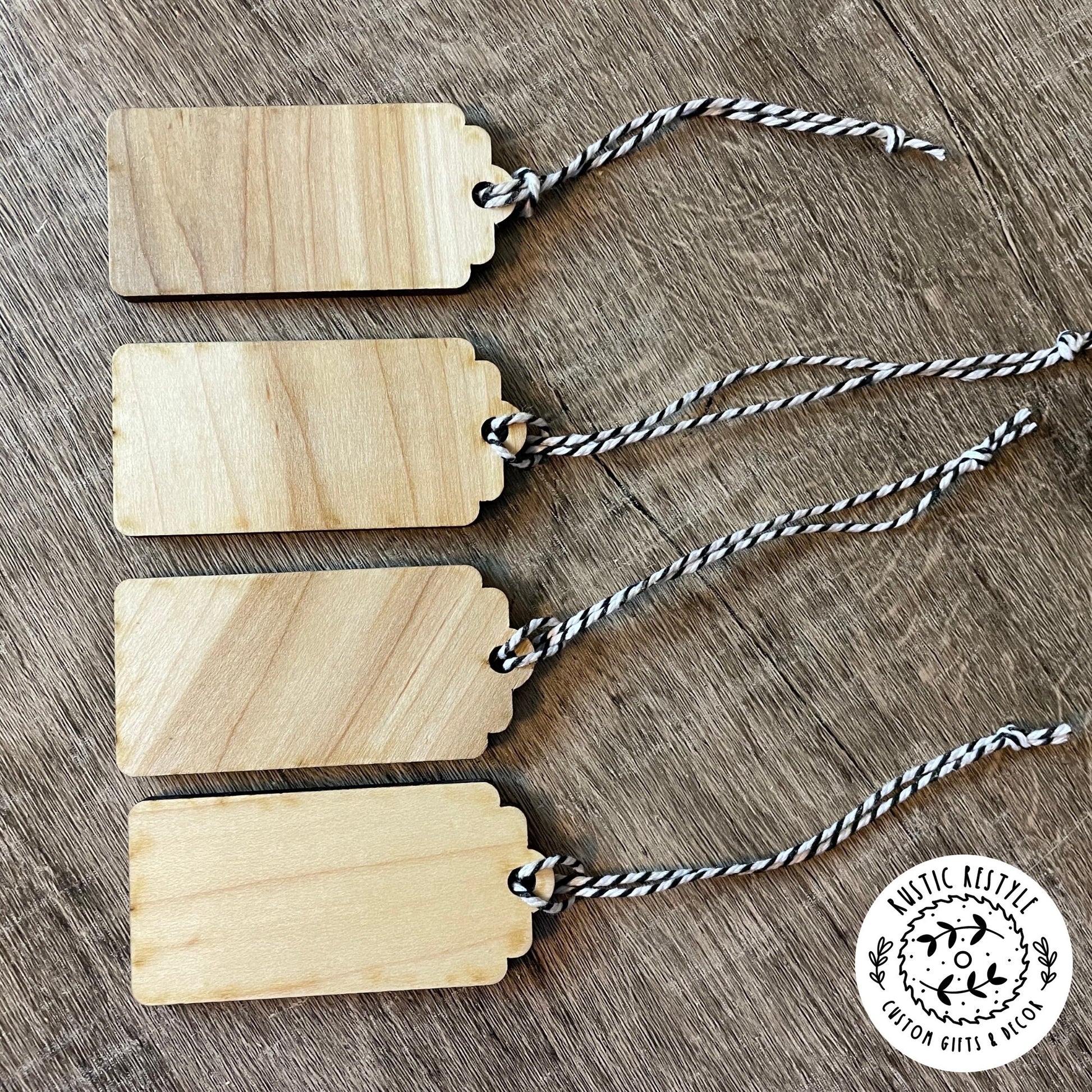 4 Christmas gift tags laying on a wooden table. This photo shows the back side of the tags all blank with wood grain. Each tag has a black and white bakers twine string.