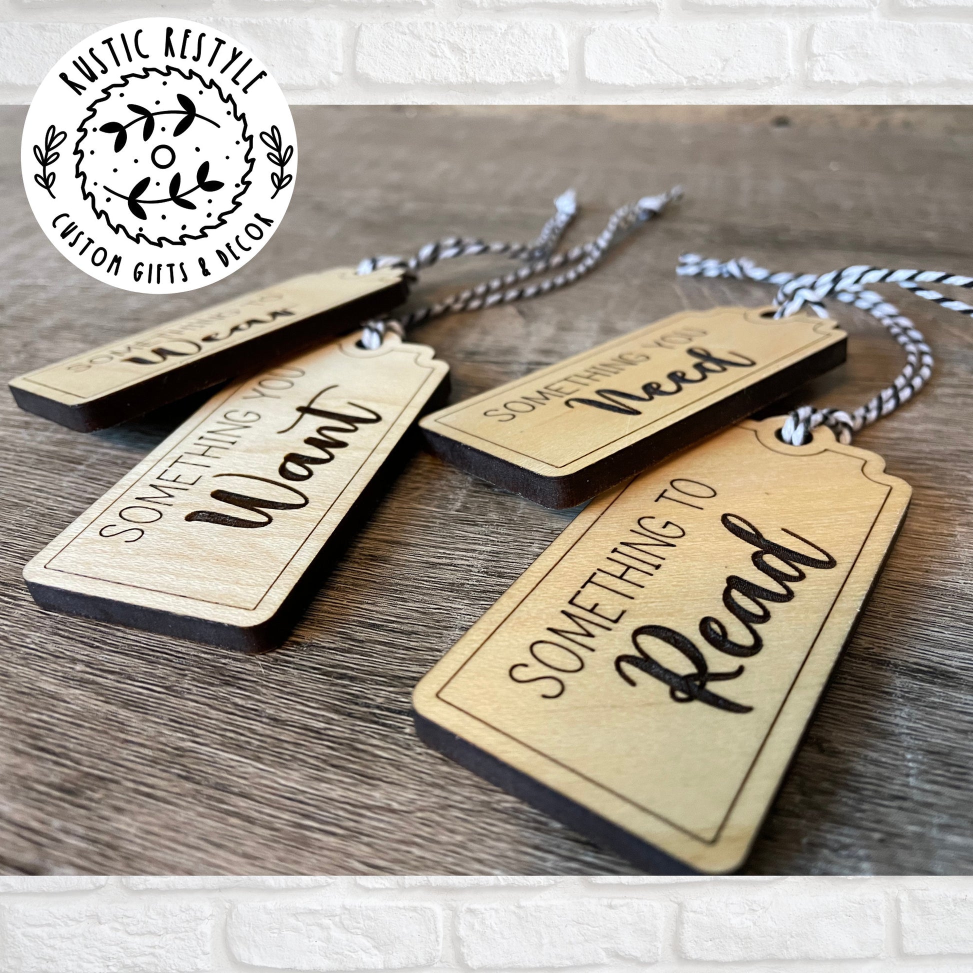 4 Christmas gift tags laying on a wooden table. First tag says Something you Need. Second tag says Something you Want. Third tag says Something you Read and the last tag says something you Wear. Each tag has a black and white bakers twine string.